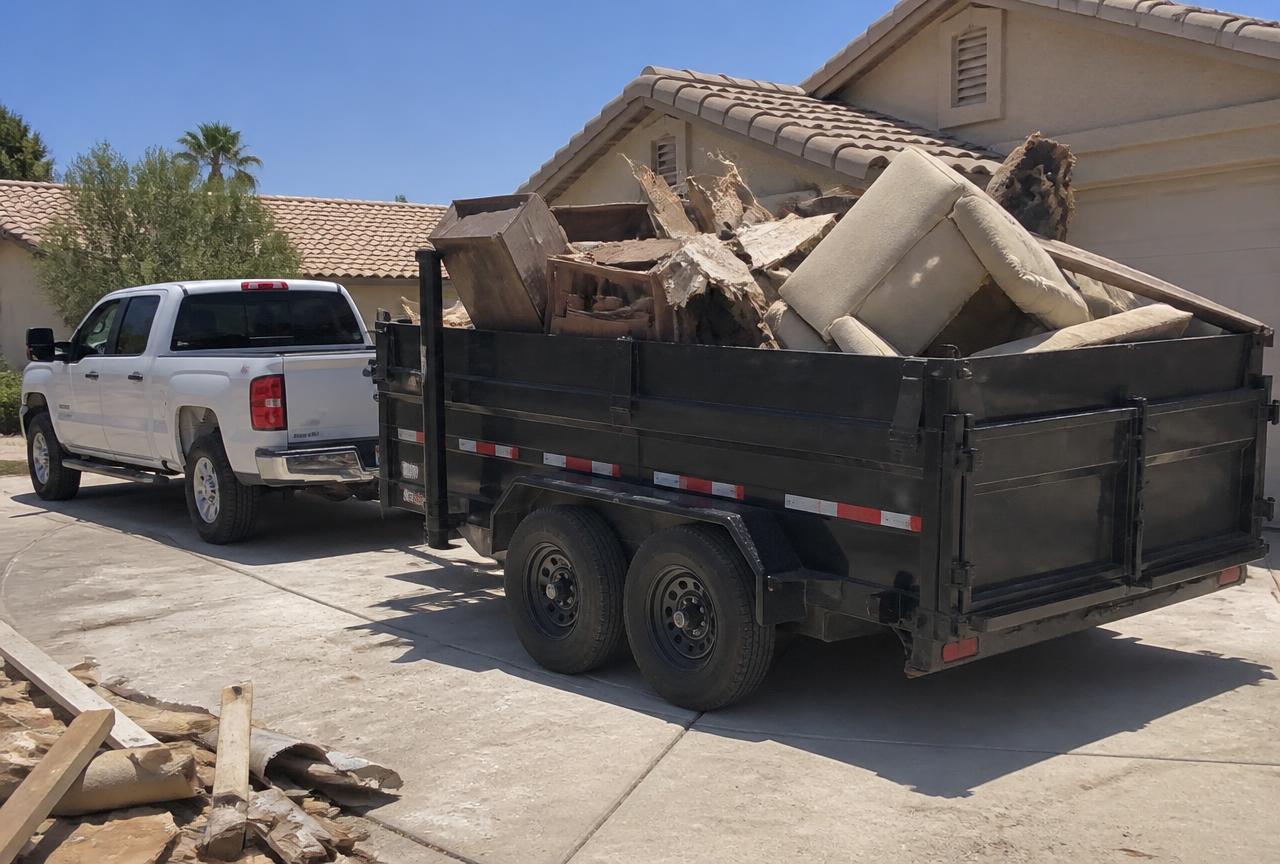 Household junk and debris loaded into a dump trailer behind a pickup truck